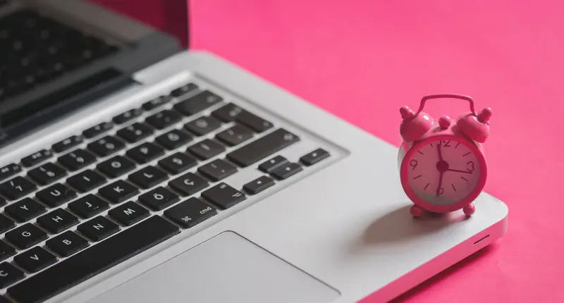 Laptop with a clock on it on a pink table